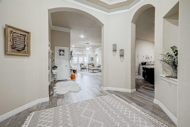 entrance foyer featuring ornamental molding, arched walkways, baseboards, and wood finished floors