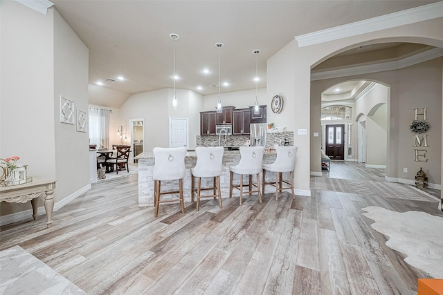 kitchen featuring arched walkways, a breakfast bar area, dark brown cabinets, appliances with stainless steel finishes, and decorative backsplash