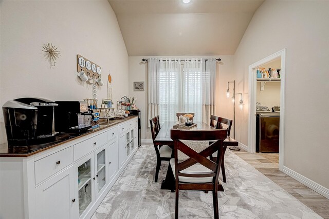 dining room featuring lofted ceiling, light wood-type flooring, washing machine and clothes dryer, and baseboards