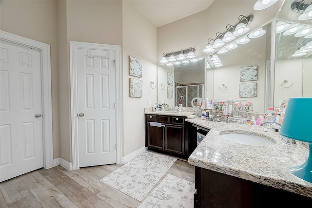 full bath featuring a stall shower, vanity, baseboards, and wood finished floors