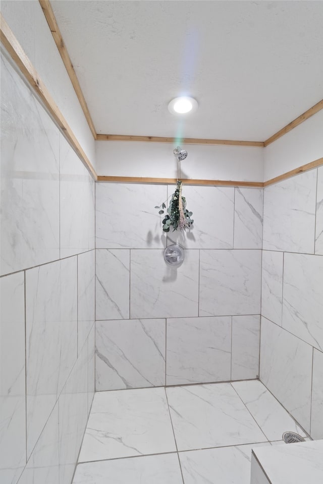 bathroom with a tile shower and crown molding