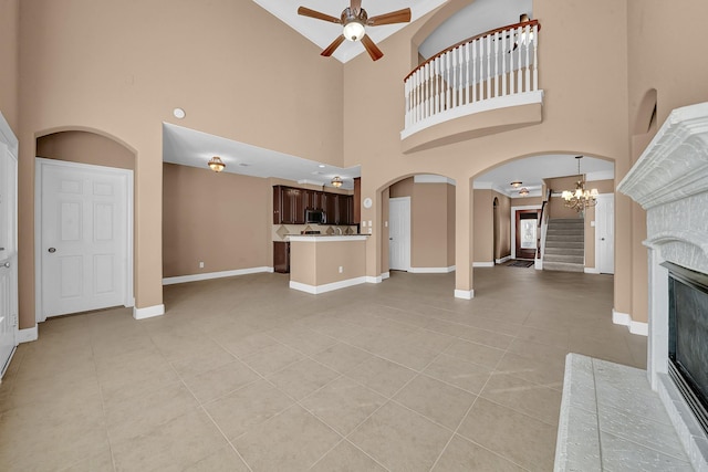 unfurnished living room featuring ceiling fan with notable chandelier, a towering ceiling, a fireplace, and light tile patterned floors