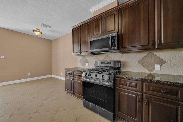 kitchen featuring light tile patterned floors, stainless steel appliances, dark brown cabinets, and dark stone counters