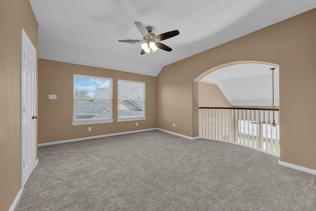 empty room with a wealth of natural light, ceiling fan, light colored carpet, and vaulted ceiling