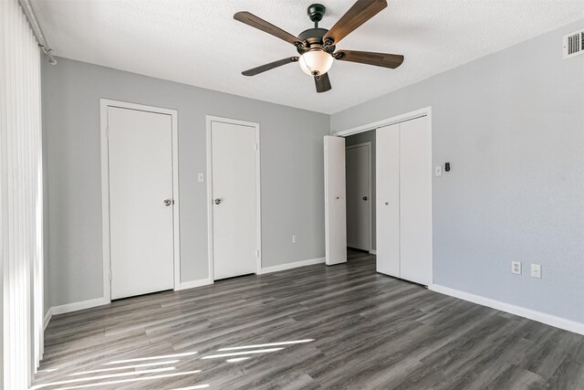 unfurnished bedroom with ceiling fan, dark hardwood / wood-style floors, a textured ceiling, and multiple closets