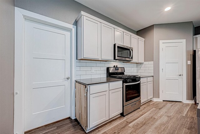 kitchen with appliances with stainless steel finishes, white cabinetry, decorative backsplash, and light hardwood / wood-style floors