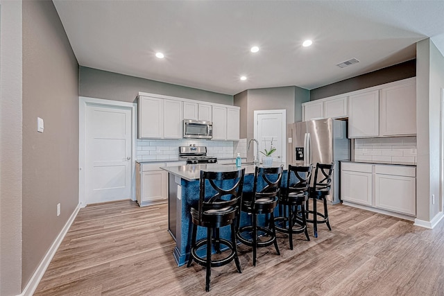 kitchen featuring tasteful backsplash, stainless steel appliances, white cabinets, and an island with sink