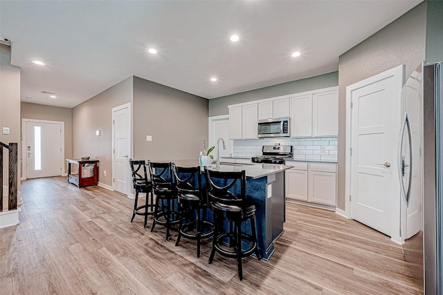 kitchen with sink, white cabinetry, light hardwood / wood-style flooring, a center island with sink, and appliances with stainless steel finishes