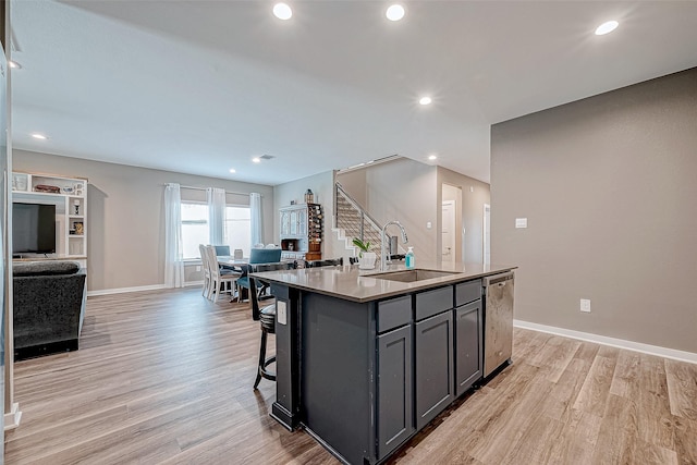 kitchen with sink, light wood-type flooring, stainless steel dishwasher, gray cabinets, and a kitchen island with sink