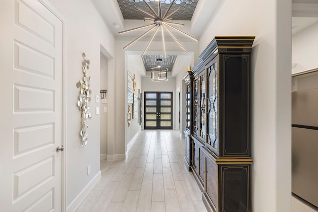 corridor featuring a tray ceiling, french doors, and a notable chandelier