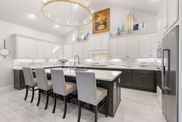 kitchen with a breakfast bar, a kitchen island with sink, vaulted ceiling, white cabinetry, and stainless steel appliances