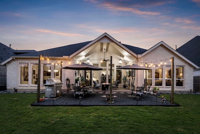 back house at dusk featuring a lawn and a patio area