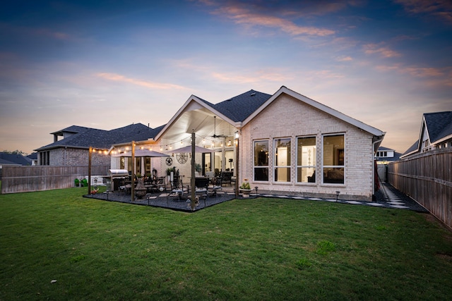 back house at dusk with a lawn, a patio area, and ceiling fan