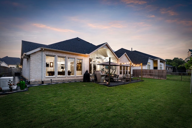 back house at dusk featuring a lawn, ceiling fan, central AC unit, and a patio area