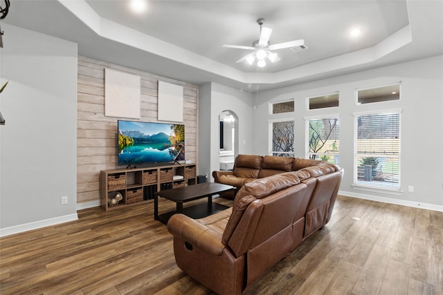 living room featuring hardwood / wood-style flooring, ceiling fan, a tray ceiling, and wood walls