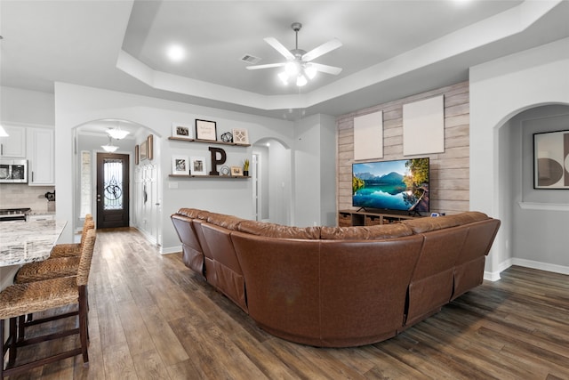 living room featuring ceiling fan, a tray ceiling, and dark wood-type flooring