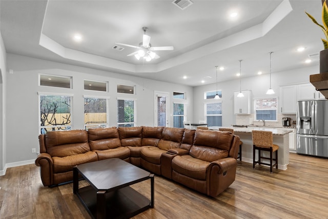 living room featuring ceiling fan, light wood-type flooring, and a raised ceiling