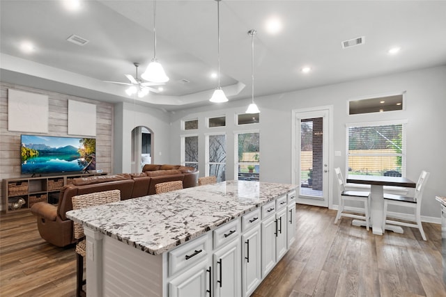 kitchen featuring white cabinetry, a center island, ceiling fan, hanging light fixtures, and a tray ceiling