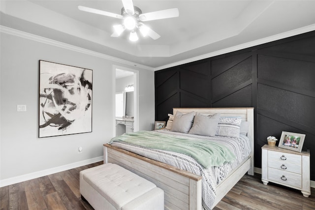 bedroom with ensuite bath, a raised ceiling, ceiling fan, dark hardwood / wood-style flooring, and crown molding