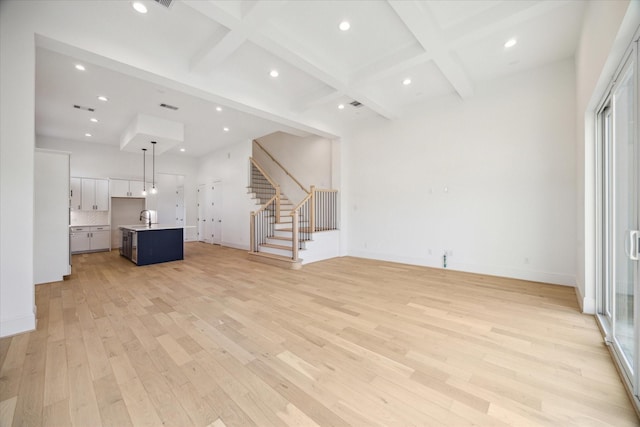 unfurnished living room featuring beamed ceiling, coffered ceiling, sink, and light hardwood / wood-style flooring