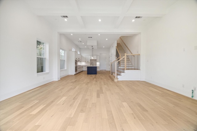 unfurnished living room featuring beam ceiling, light wood-type flooring, and coffered ceiling