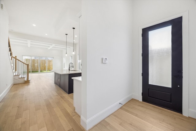 foyer entrance with beam ceiling, light wood-type flooring, coffered ceiling, and sink