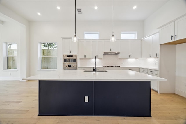 kitchen with a kitchen island with sink, white cabinets, sink, light stone countertops, and decorative light fixtures