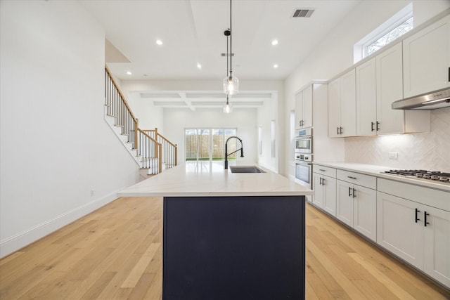 kitchen with pendant lighting, a kitchen island with sink, sink, appliances with stainless steel finishes, and beam ceiling