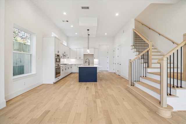 kitchen with stainless steel gas cooktop, an island with sink, light hardwood / wood-style floors, decorative light fixtures, and white cabinets