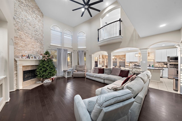 living room with ceiling fan, light wood-type flooring, a towering ceiling, and a fireplace