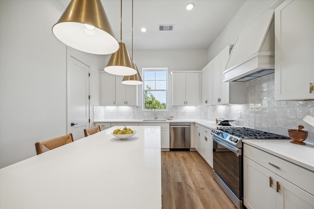 kitchen with pendant lighting, custom exhaust hood, white cabinets, sink, and stainless steel appliances