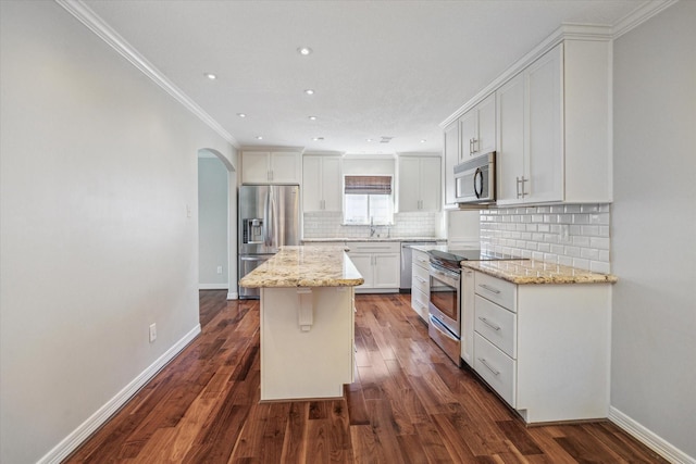 kitchen with white cabinets, light stone counters, appliances with stainless steel finishes, a kitchen island, and dark hardwood / wood-style flooring