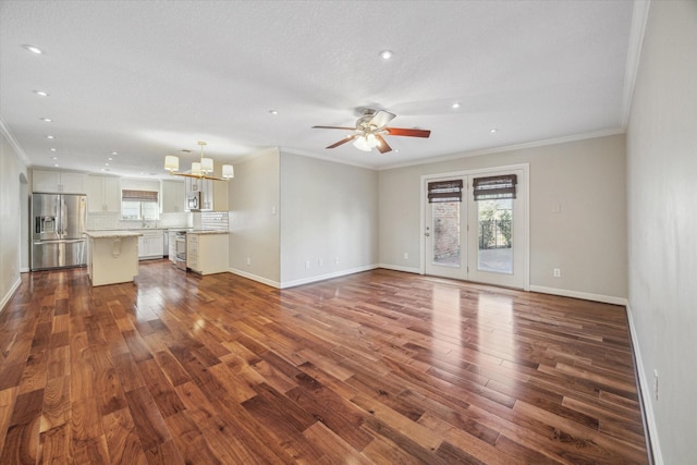 unfurnished living room featuring ceiling fan with notable chandelier, ornamental molding, and dark wood-type flooring