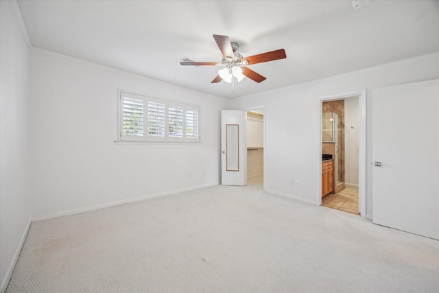 unfurnished bedroom featuring a spacious closet, ceiling fan, ensuite bathroom, and light colored carpet