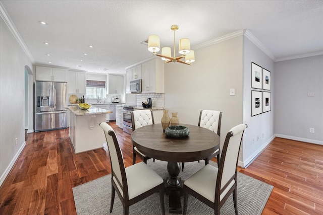 dining area with hardwood / wood-style floors, sink, ornamental molding, and an inviting chandelier