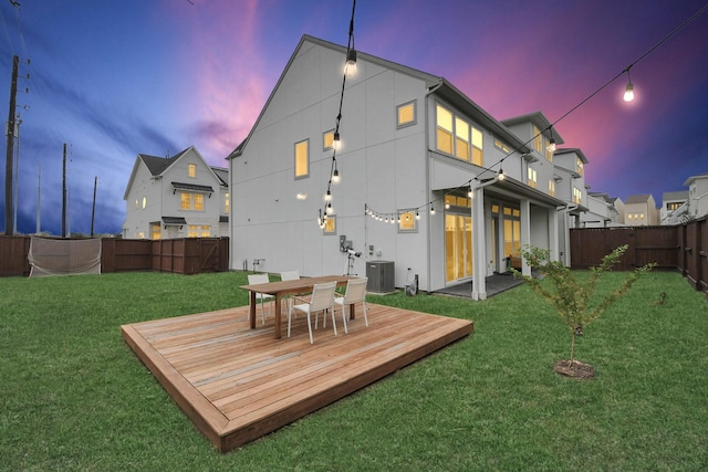 back house at dusk with a lawn, a wooden deck, and central AC