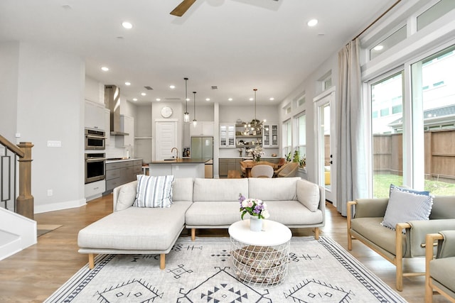 living room with ceiling fan, sink, and light wood-type flooring