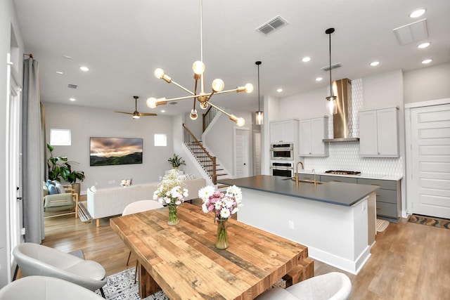 kitchen with pendant lighting, gray cabinetry, a kitchen island with sink, wall chimney exhaust hood, and tasteful backsplash