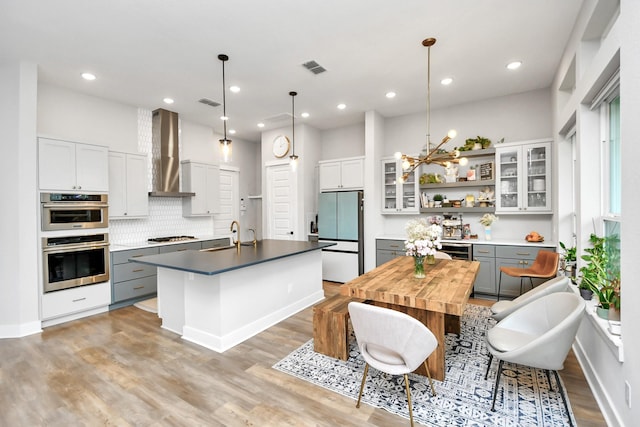 kitchen with appliances with stainless steel finishes, gray cabinets, a center island with sink, and wall chimney range hood