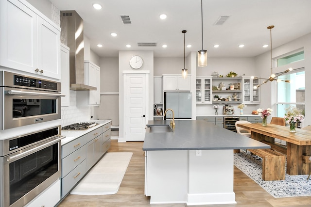 kitchen with a kitchen island with sink, hanging light fixtures, decorative backsplash, white cabinetry, and stainless steel appliances