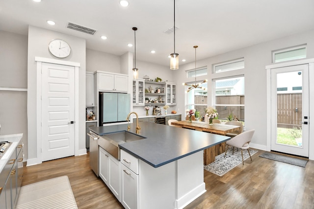 kitchen featuring a wealth of natural light, white cabinetry, stainless steel appliances, an island with sink, and decorative light fixtures