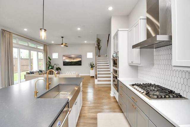 kitchen featuring sink, hanging light fixtures, wall chimney range hood, backsplash, and appliances with stainless steel finishes