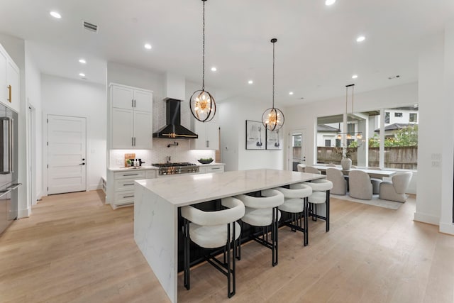 kitchen with white cabinets, a large island, light stone countertops, and wall chimney range hood