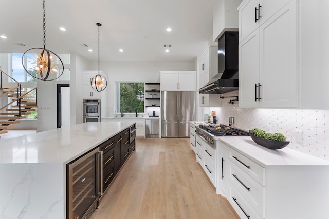 kitchen with stainless steel appliances, wall chimney range hood, wine cooler, decorative light fixtures, and white cabinets