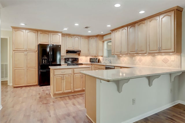 kitchen featuring a kitchen breakfast bar, kitchen peninsula, light hardwood / wood-style flooring, and black appliances