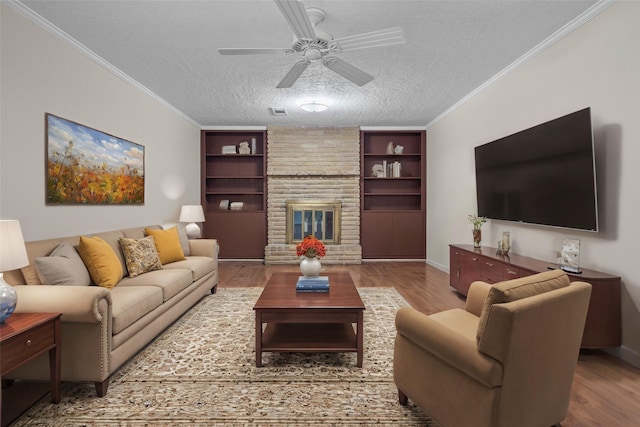 living room with ornamental molding, built in shelves, a textured ceiling, a fireplace, and light hardwood / wood-style floors