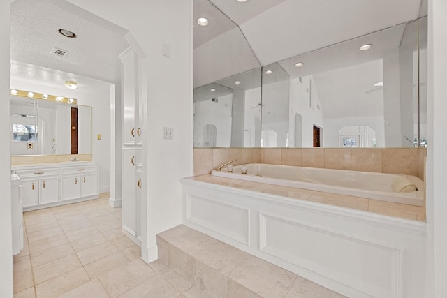 bathroom with a textured ceiling, a tub, vanity, and lofted ceiling