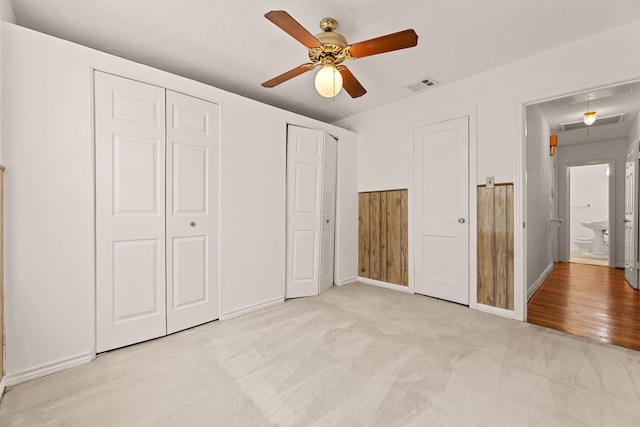 unfurnished bedroom featuring ceiling fan, light colored carpet, ensuite bath, and two closets