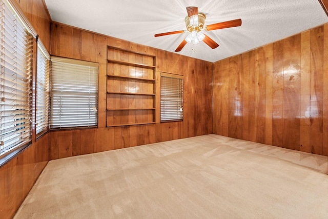 carpeted spare room with wooden walls, ceiling fan, and a textured ceiling