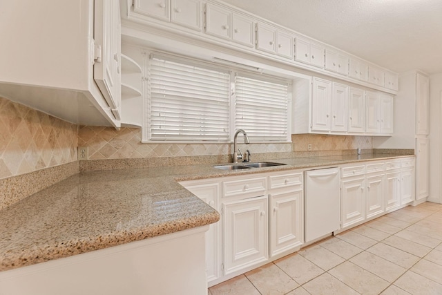 kitchen with dishwasher, sink, light stone countertops, light tile patterned floors, and white cabinetry